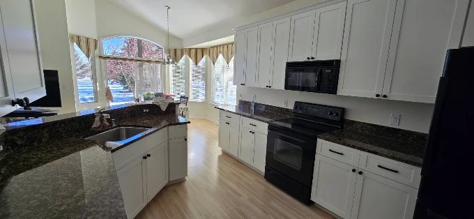 White cabinets with dark granite countertops in a bright corner kitchen