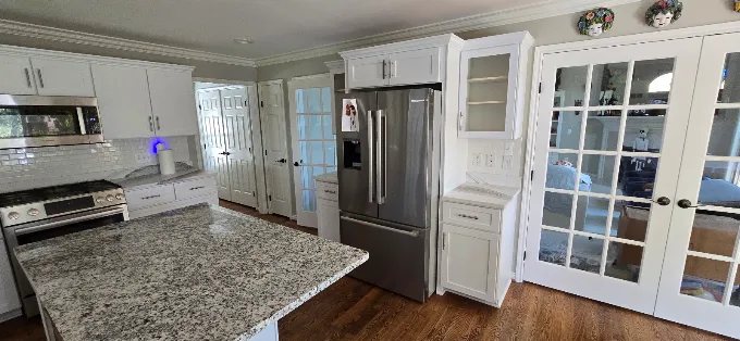 Built-in refrigerator surround with custom white cabinets and granite island