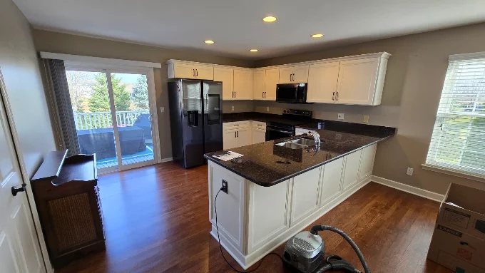 Kitchen peninsula with granite countertop, white cabinets, and hardwood floors